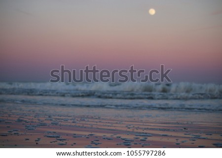 Beautiful sunset gradient on the beach in Pawleys Island, South Carolina - purple, pink, orange, and yellow gradient blurred in background with focus on the reflection of the color in the bubbly sand