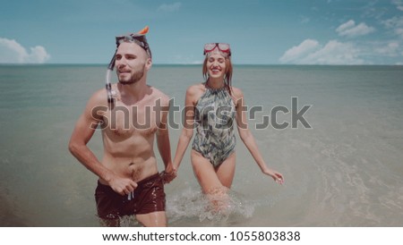 Young happy couple with snorkeling masks having fun in the sea water, enjoying sunny summer day on their beach tropical holiday