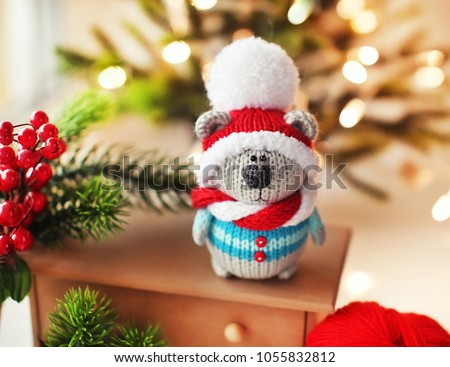 Handmade knitted toy. Christmas bear in striped sweater and red and white scarf, on the background of Christmas lights and green branches