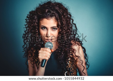 Woman unhappy talking by microphone looking skeptical to you camera isolated blue background. Negative face expression, human emotion, reaction, attitude