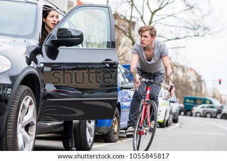 Angry young bicyclist shouting while swerving for avoiding dangerous collision with the open door of a 4x4 car on a busy street in the city Royalty-Free Stock Photo #1055845817