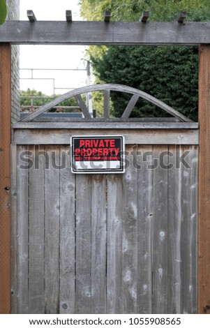 Red and black Private Property No Trespassing sign, on a wooden gate to a residential backyard