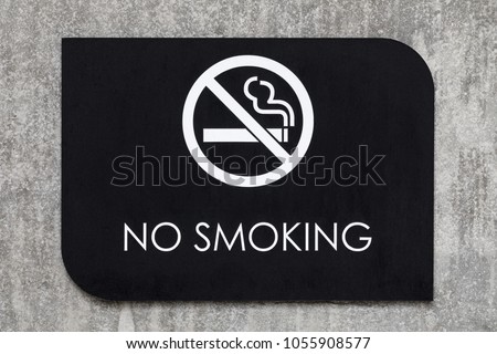 Extreme close up on a black No Smoking sign, with a cigarette symbol in white, on a concrete wall