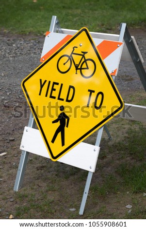 Side view on a yellow Bicycle Riders Yield to Pedestrians sign, on an easel along a gravel trail at a public park