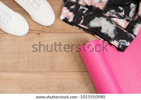 Fashion trendy trainers and leggings, pink yoga mat. Hipster Set. Female sneakers, sport shoes in flat lay style, top view. Fitness concept, active lifestyle, body care concept. Wood Background