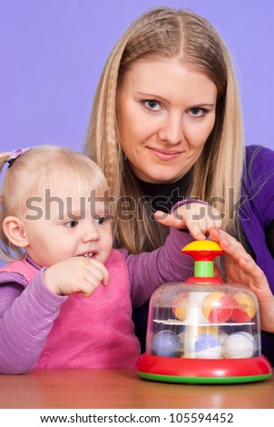 A good Caucasian mother with her daughter at the table with a toy on a violet background