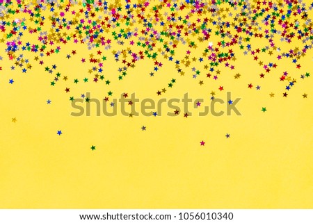 Scattered star shaped colorful glittering confetti over yellow background. Copy space.