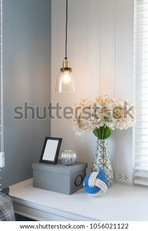 Desk with blank white picture frame placed on wooden box with flower vase