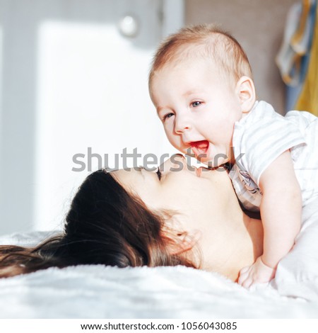 Portrait of mother and baby playing and smiling at home. Lying on bed, happy baby