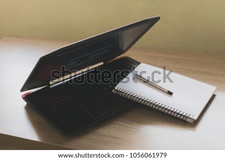 Picture showing a note-book with a pen kept on top of the keyboard of a laptop.