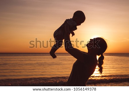 Mother and baby son  playing on the beach at the sunset time. People having fun outdoors. Concept of summer vacation and friendly family.
