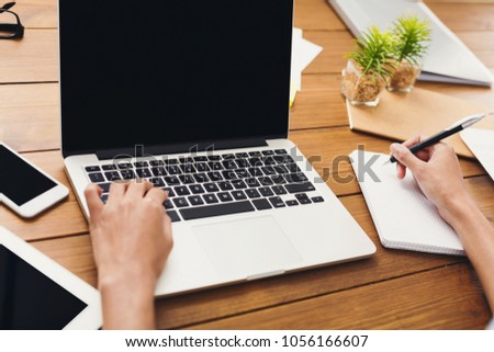 Unrecognizable businesswoman using laptop with blank screen and writing notes, copy space