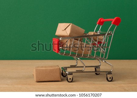 Miniature toy shopping cart with parcels on green background, business, shopping concept. Mockup for advertising of gifts, clothing, shopping, copy space.