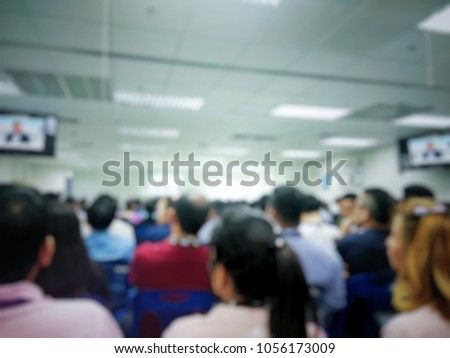 Blurred photo of many people in the meeting in the hall with fluorescent light on the ceil.