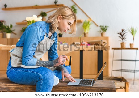 side view of young florist holding credit card and using laptop