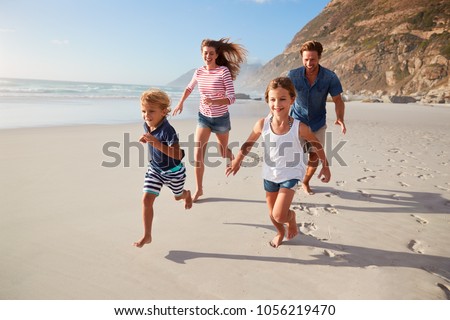 Parents Running Along Beach With Children On Summer Vacation Royalty-Free Stock Photo #1056219470