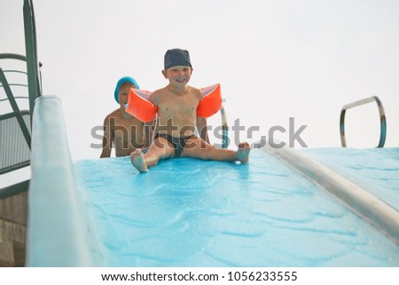 child in armlets for swimming in an outdoor pool with a water slide
