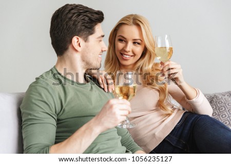 Picture of smiling young loving couple indoors at home drinking alcohol white wine champagne.