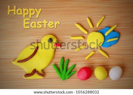 Funny spring Happy Easter image made of plasticine / Yellow chicken, green grass, colorful eggs - red, yellow and white, golden sun shining over blue cloud on wooden background, writing, sign