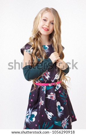 Beautiful little blonde girl with long wavy hair in fashionable black dress posing in studio over white background