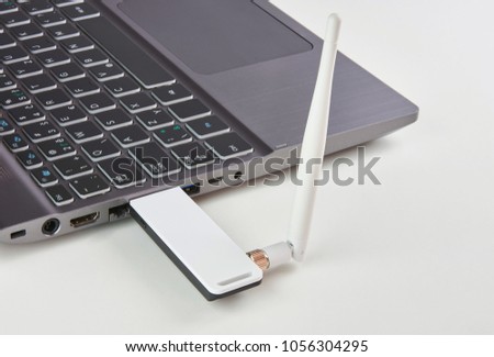 Silver laptop with USB modem plugged in with an antenna, on a white board table Royalty-Free Stock Photo #1056304295