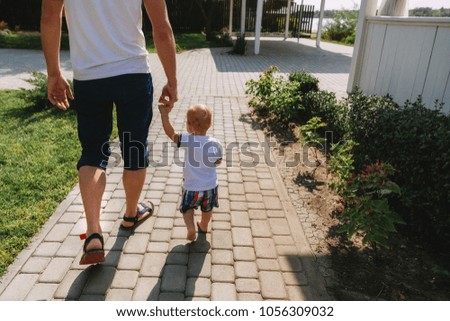 The father walks with his young son in the summer along the stone path in the park, the father holds the little son by the hand
