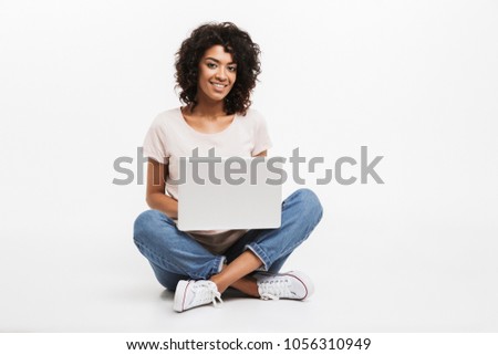 Portrait of smiling young afro american woman using laptop while sitting on a floor with legs crossed isolated over white background