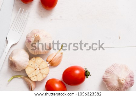 Bunch of tomatoes stock images. White fork knife plate on an old wooden plank tray. Art idea white tomatoes, painted with paint. Bright spot three red tomatoes. Garlic for cooking art  abstract absurd
