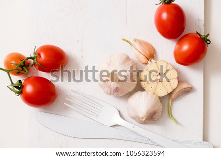 Bunch of tomatoes stock images. White fork knife plate on an old wooden plank tray. Art idea white tomatoes, painted with paint. Bright spot three red tomatoes. Garlic for cooking Fresh red tomatoes