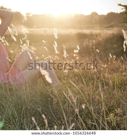 one beautiful blond girl in pink dress is siting on the field of spikelets in the sunset
