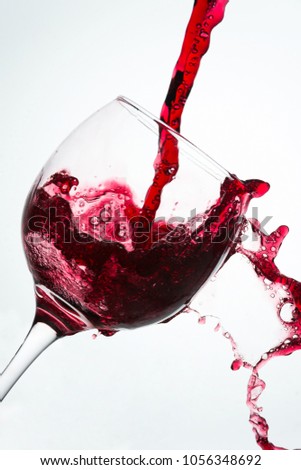 Close up of the pouring with spill of red wine on a glass against a white background