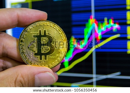 Man's hand holding Golden Bitcoin with stock exchange market graph background. Digital money trading concept.