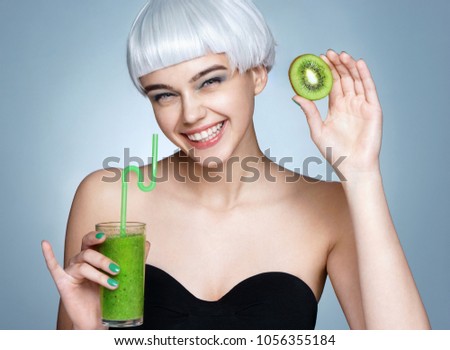 Smiling young girl holding smoothie detox cocktail of kiwi fruit. Photo of fashion model on blue background. Healthy lifestyle