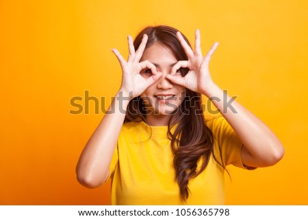 Asian woman do funny  double OK sign as glasses in yellow dress on yellow background