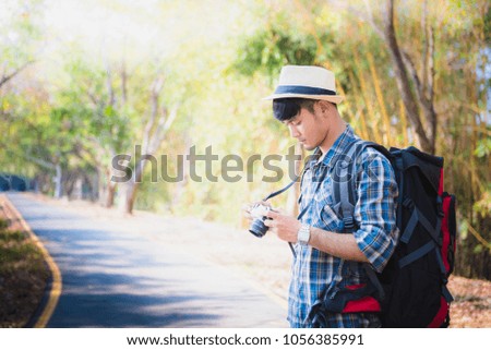 backpack young man traveler photographing holding digital camera on the road in the forest.
