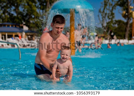 Young active father playing with a cute baby, happy laughing boy, enjoying a hot summer day in an outdoor pool of a resort during vacation