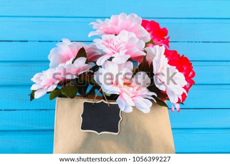 Pink peonies in a craft package with a chalkboard on a blue wooden table. Postcard for the holiday. Copy the space