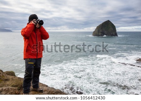 Adventurous man with a camera is standing taking pictures of the beautiful ocean during a vibrant winter morning. Taken in Cape Kiwanda, Pacific City, Oregon Coast, America.