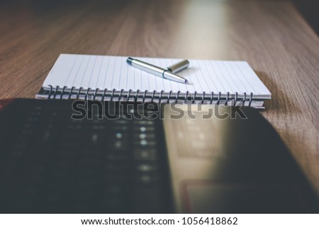 Pen with an open cap kept on a notebook on a wooden office table near a laptop for business purpose.