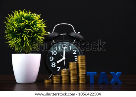 Time to pay TAX concept. TAX alphabet with stack of coin and vintage alarm clock in dark background, business and financial concept idea.