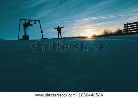 A guy with his arms spread on the top of a mountain surrounded by snow. The sunset.Motivation photo