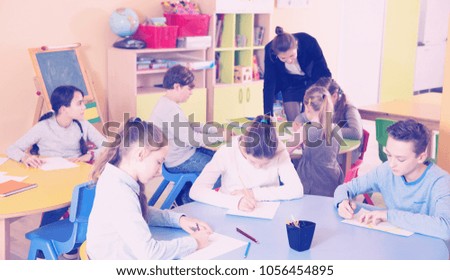 Smiling boys and girls studying and teacher helping at class