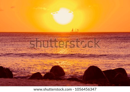 bright and colorful sunset on the Caribbean beach in Aruba island in winter with people on the white beach and palm trees