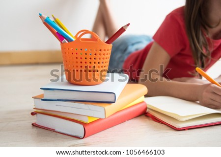 Homeschooling. The child, the pupil, the schoolgirl lies on a floor with a pile of books and writes homework. Education of children. Training of children in kindergartens and schools. Royalty-Free Stock Photo #1056466103