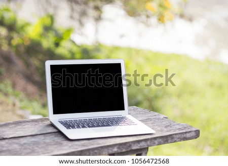 Blank screen laptop on wooden blurred nature background.
