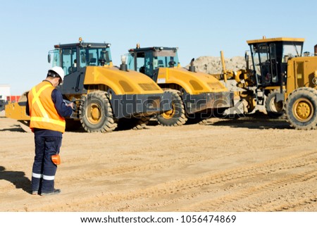 Heavy duty equipment Inspector, auditor is inspecting, checking heavy equipment on construction site. Compactor, grader, bucket loader are working on construction site. 