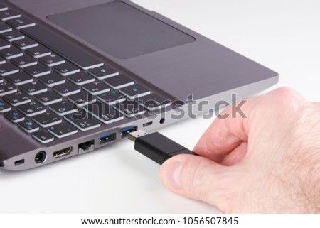 Silver laptop and male hand holding USB Flash disk and plugging into slot - on white background Royalty-Free Stock Photo #1056507845