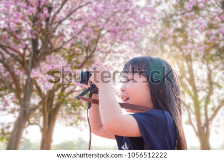 Little asian girl taking photo by camera in pink blooming flower park