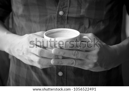 Man holding cup of coffee in his hands; picture color by black and white