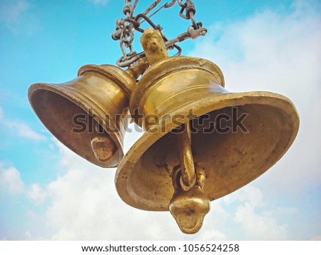 Two temple bells made of brass hanging through chain against cloudy sky. Wide and low angle view. Place: Kali Ka Tibba, Chail, Himachal Pradesh. Royalty-Free Stock Photo #1056524258
